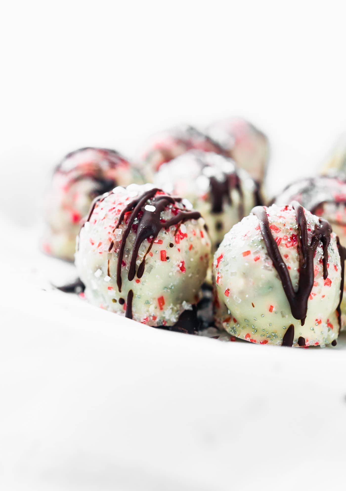 Side view white chocolate coated peppermint rum balls with red sprinkles.