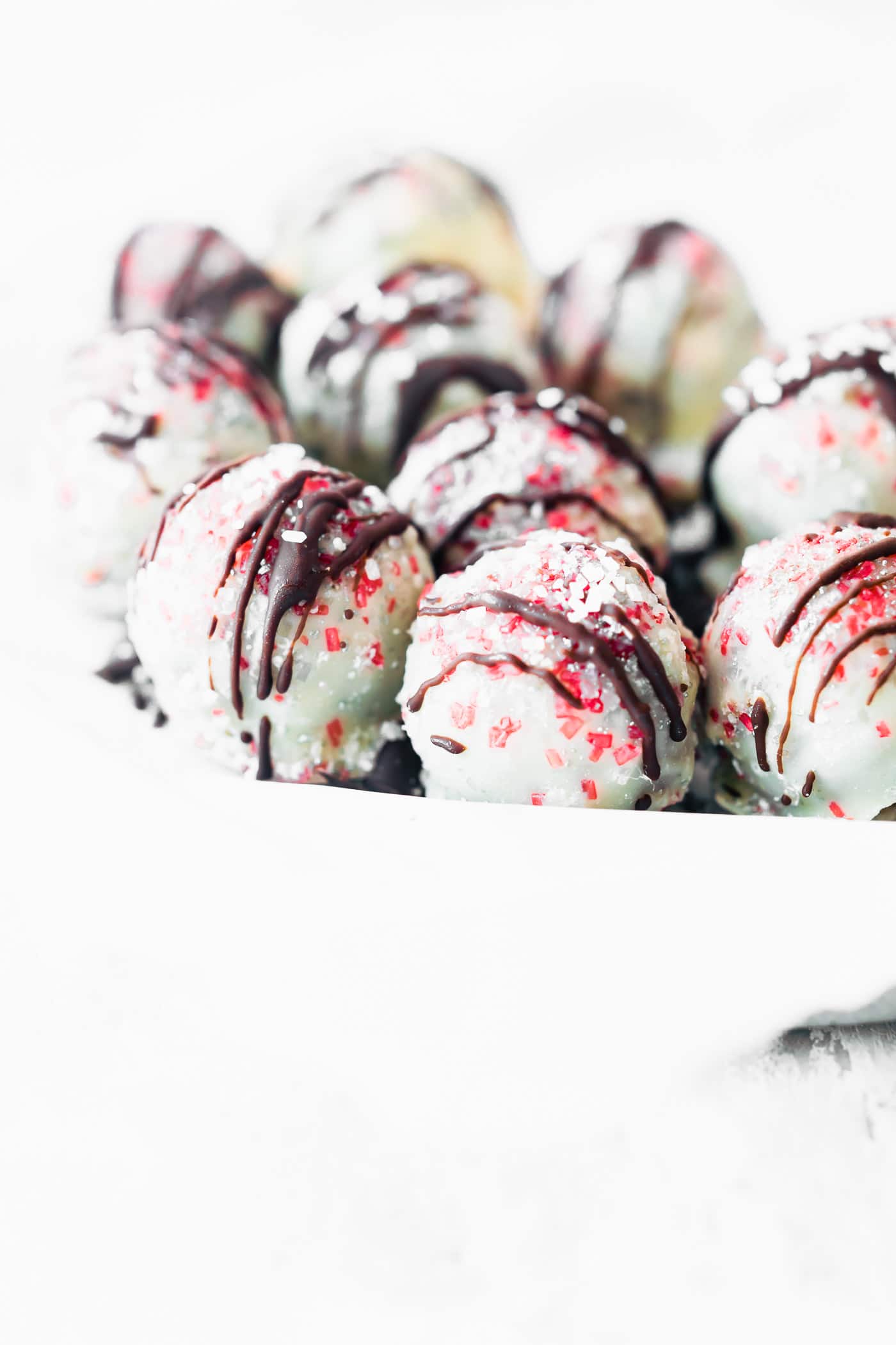 Several white chocolate coated peppermint rum balls with dark chocolate drizzled over top with red sprinkles.