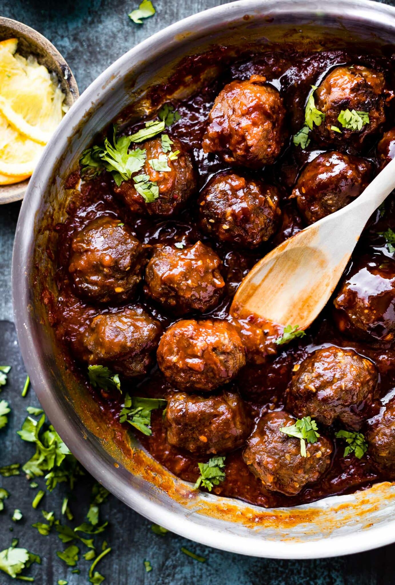 Overhead view saucy 5 Spice BBQ Meatballs in skillet with wooden spoon scooping one a meatball