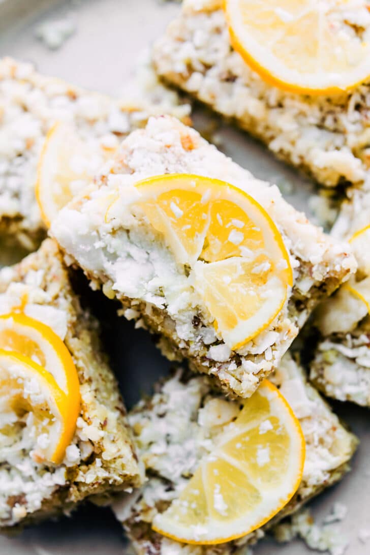 plate of no-bake lemon coconut bars, topped with coconut frosting and lemon slices.