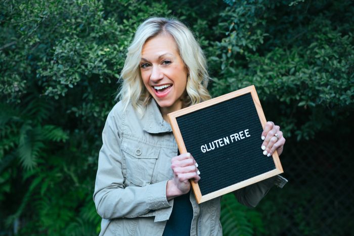 A woman with blonde hair holding sign that says 'gluten free' again greenery.
