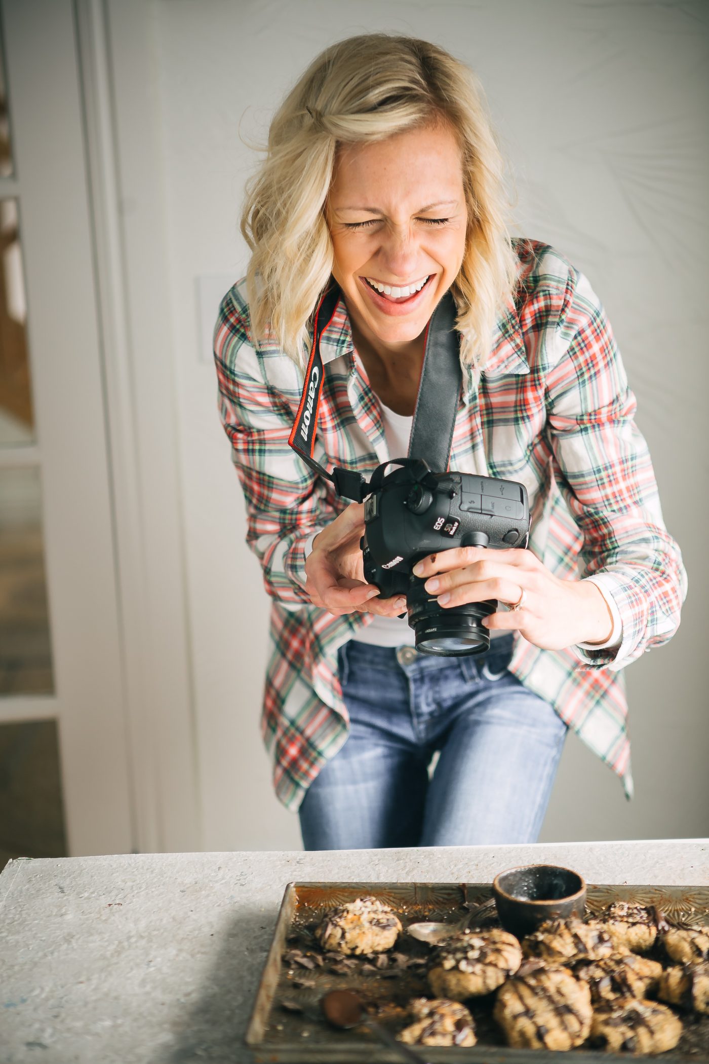 A woman laughing while holding a dslr camera above a baking sheet of food