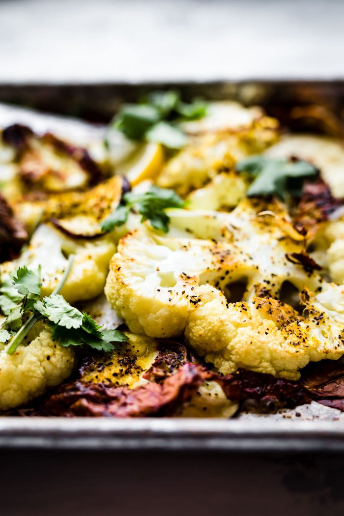 Close up view Roasted Cauliflower Steaks on baking sheet sprinkled with pepper.