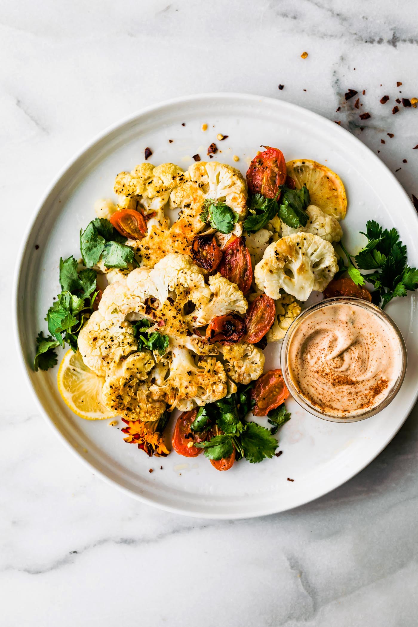 White plate with serving of roasted cauliflower steaks with extra roasted veggies, side of paprika cashew cream