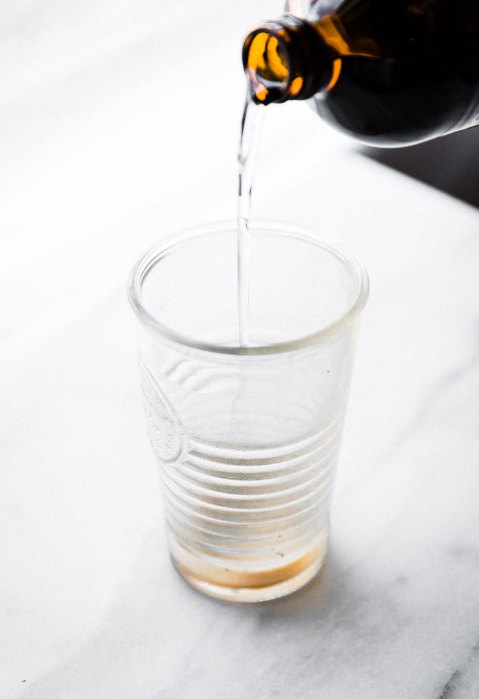 MCT oil being poured from bottle into tall clear glass for coffee drink