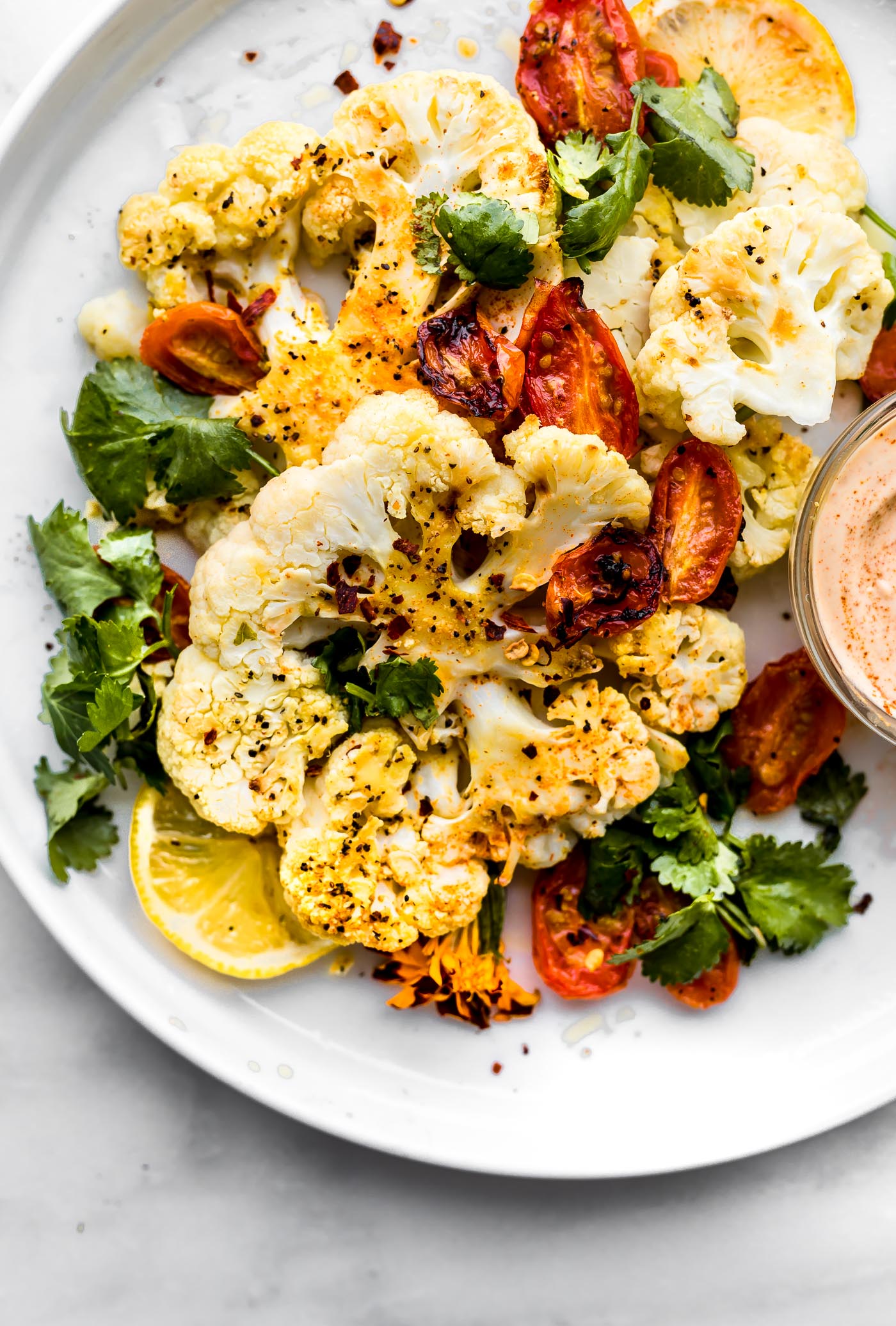 Overhead view roasted cauliflower steak with roasted vegetables side of paprika cashew cream sauce.