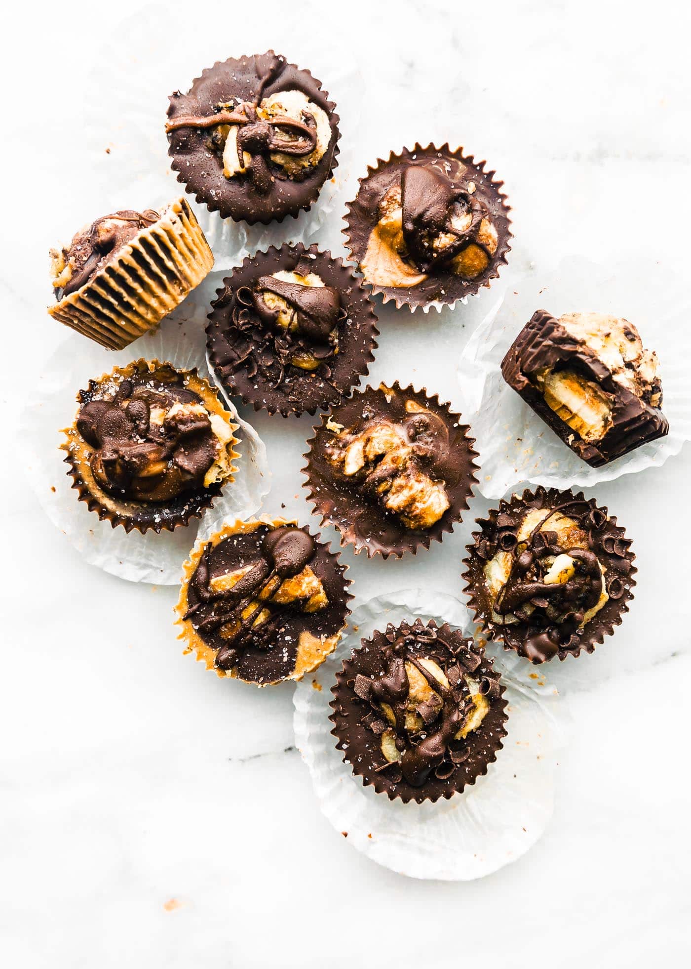 Overhead view several mini caramelized banana chocolate almond butter cups on marble background
