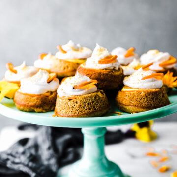 Several mini upside down cakes topped with whipped cream and orange slices on turquoise cake stand.