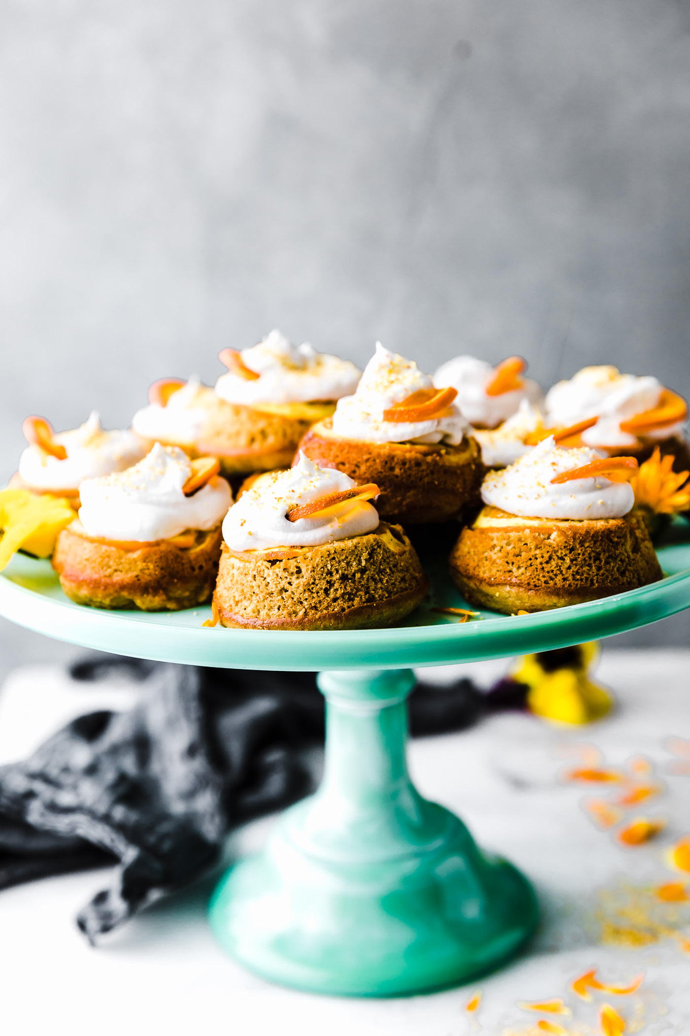 Mini orange paleo upside down cakes topped with cream and orange slice on turquoise cake stand