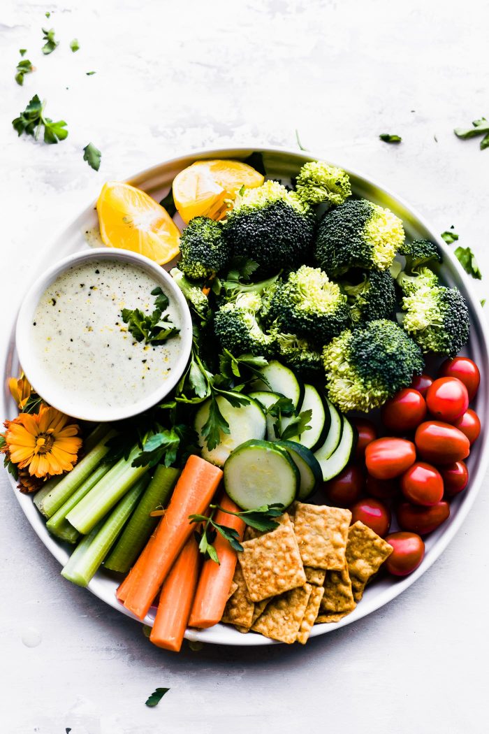 raw veggies with homemade vegan ranch dressing on round tray.