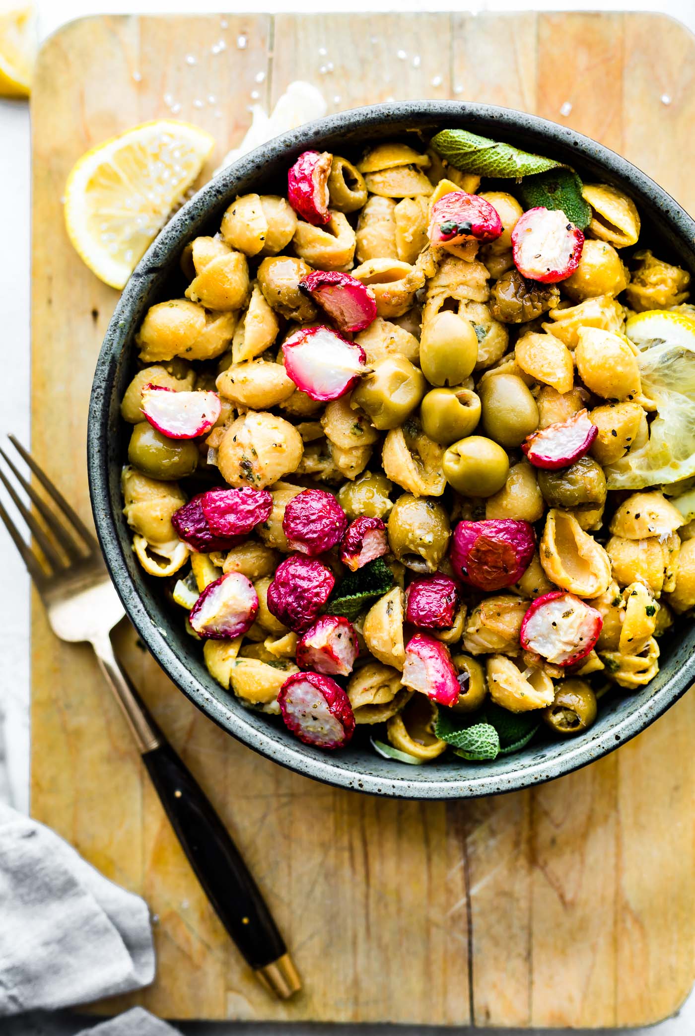 Overhead view roasted radish and chickpea pasta salad in stone bowl on wooden cutting board.