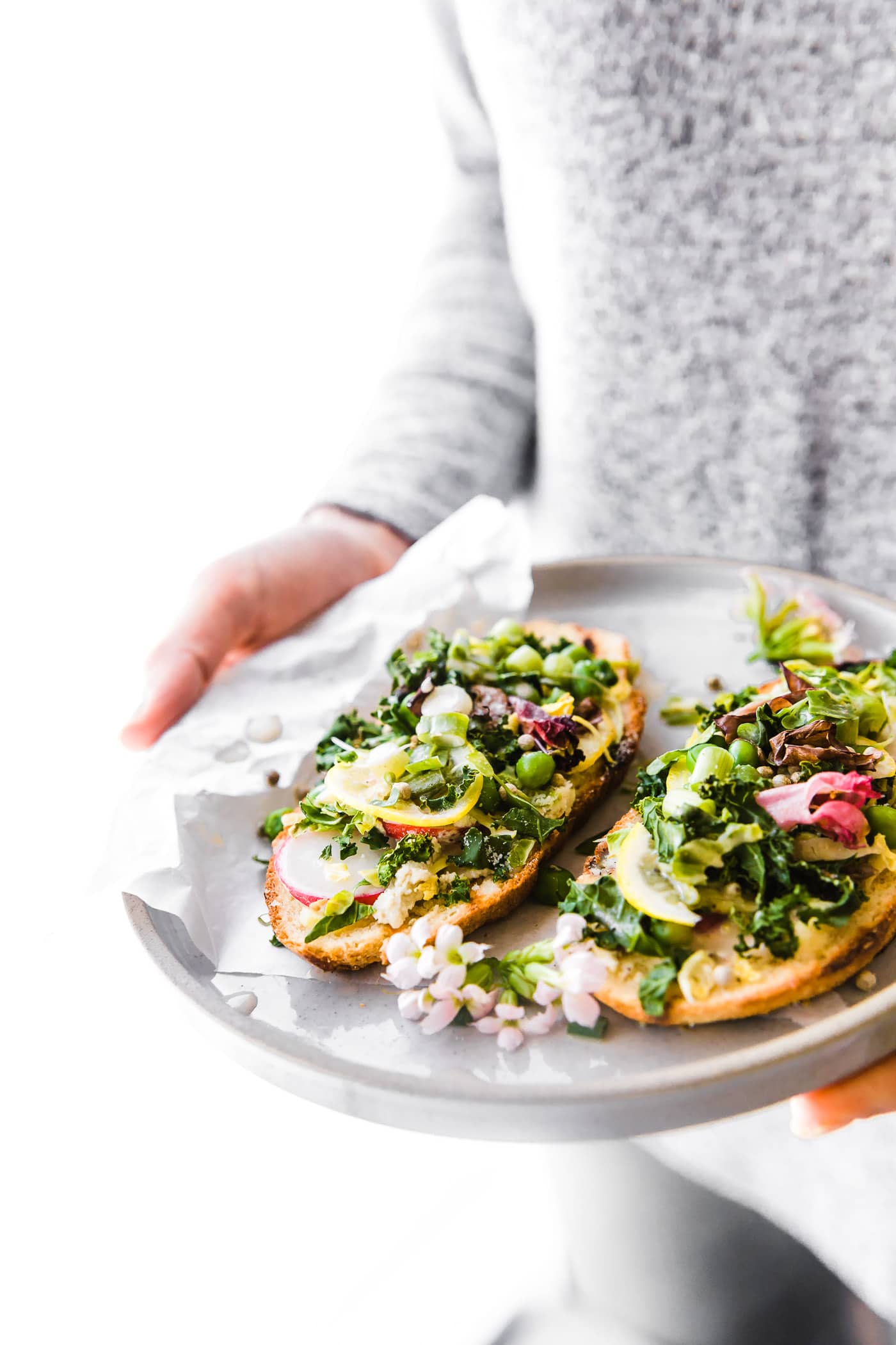 A woman holding stone plate with two pieces sourdough bread topped with spring salad mix.