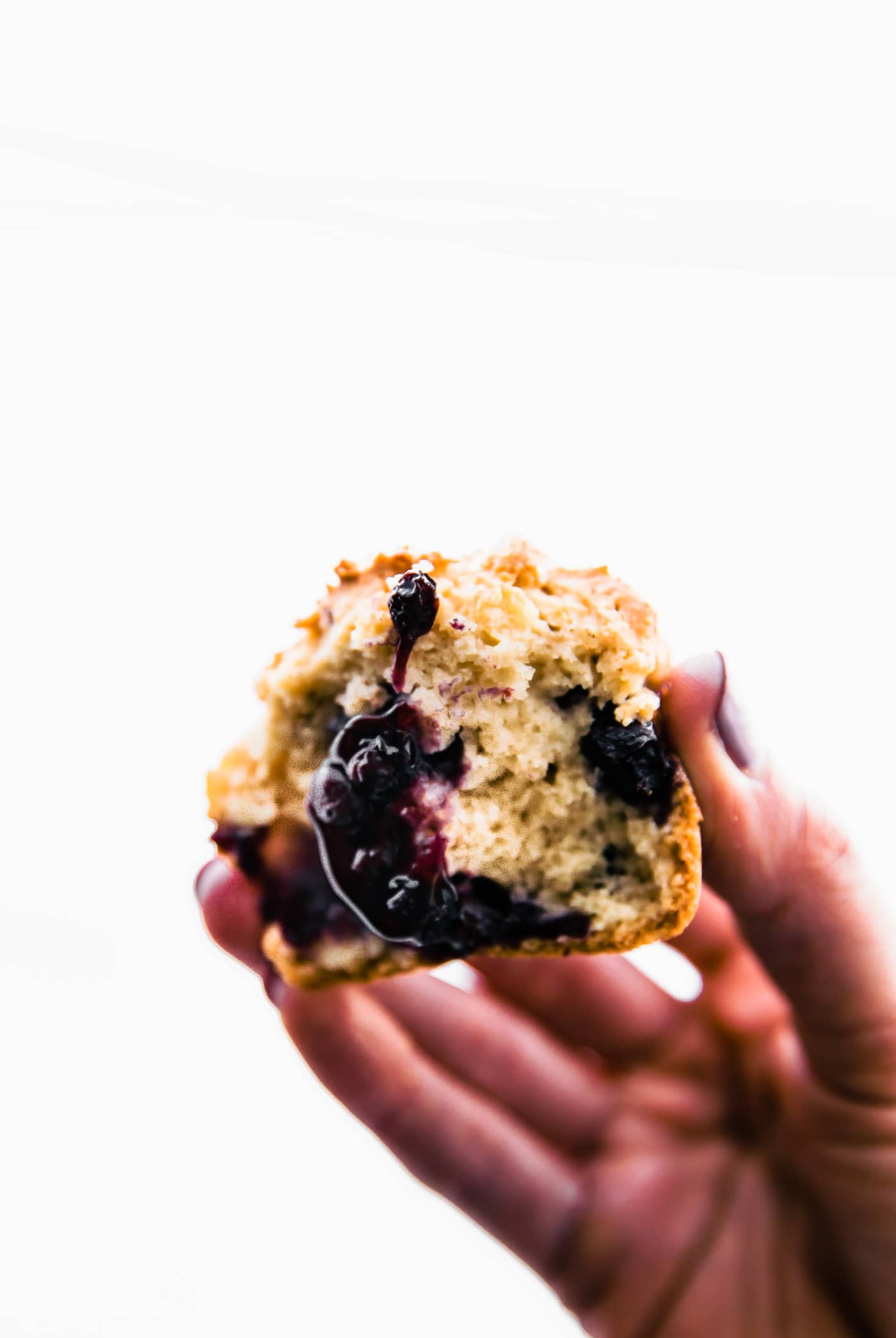 A gluten free blueberry muffin with bite taken from side being held against white background.