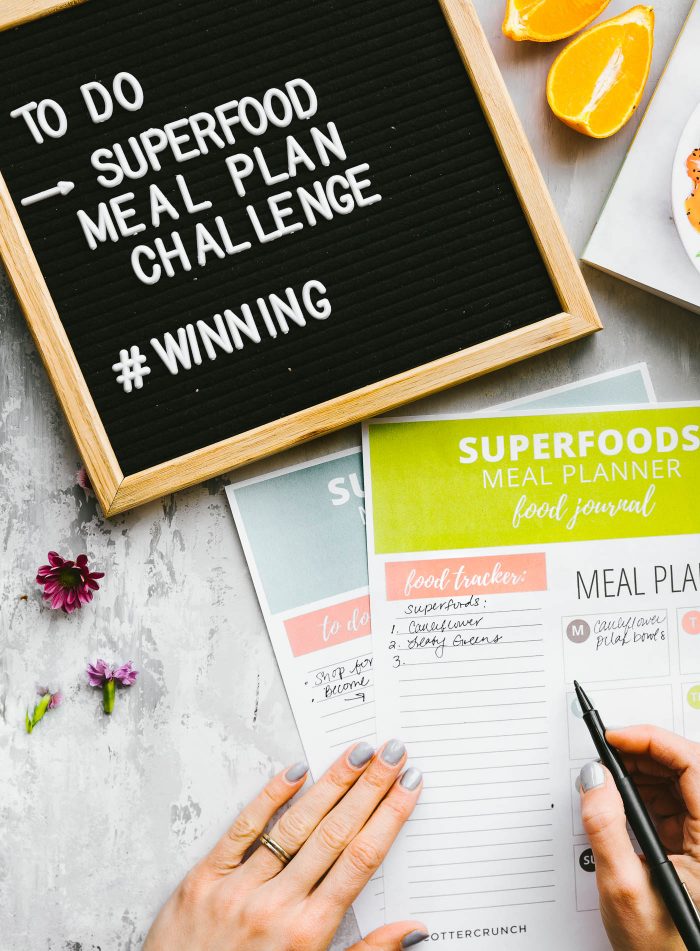 Superfoods meal planner food journals with cookbook and felt board with white words on counter.
