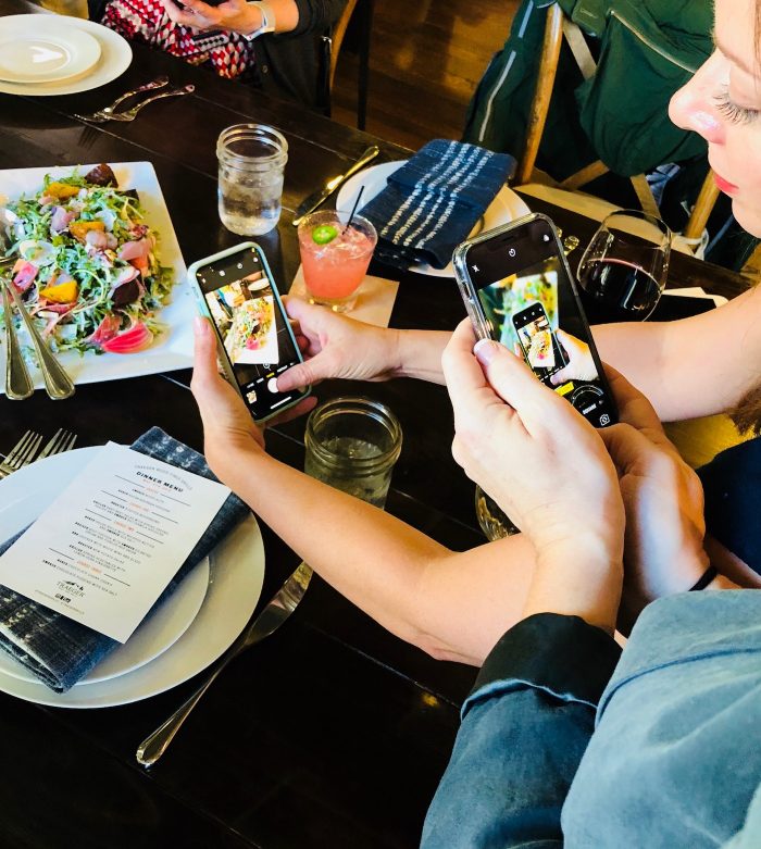 Group of women taking photos with iPhones of food on plates.
