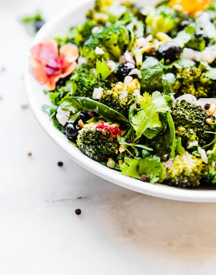 Detox Broccoli Salad in white bowl topped with fresh herbs.