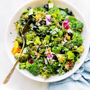 White bowl filled with detox broccoli salad with blueberries and red onions.