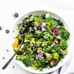 detox broccoli salad in white bowl with blueberries, broccoli, and fresh herbs.