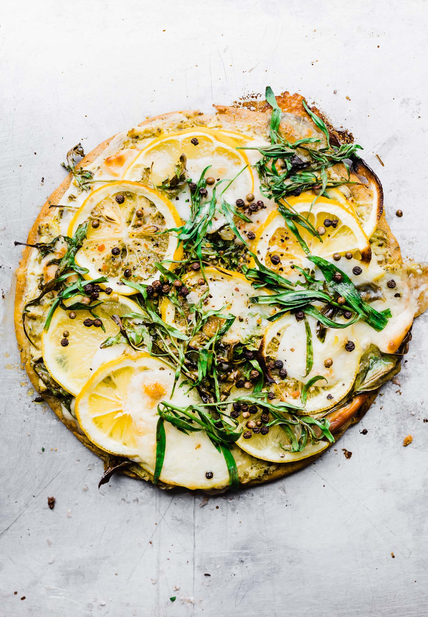 Overhead view lemon herb socca pizza topped with baked in lemon slices and fresh herbs.