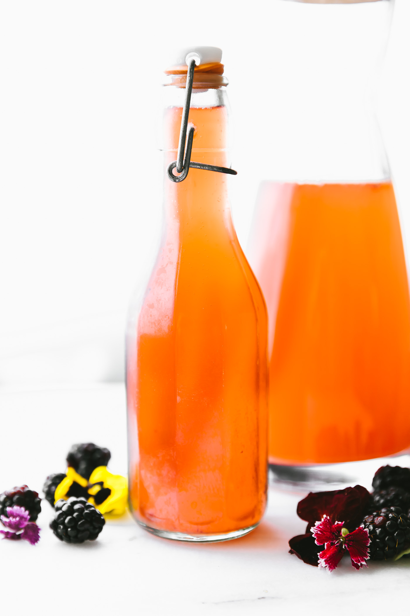 homemade Fruit kvass in glass decanter with fresh blackberries around bottles.