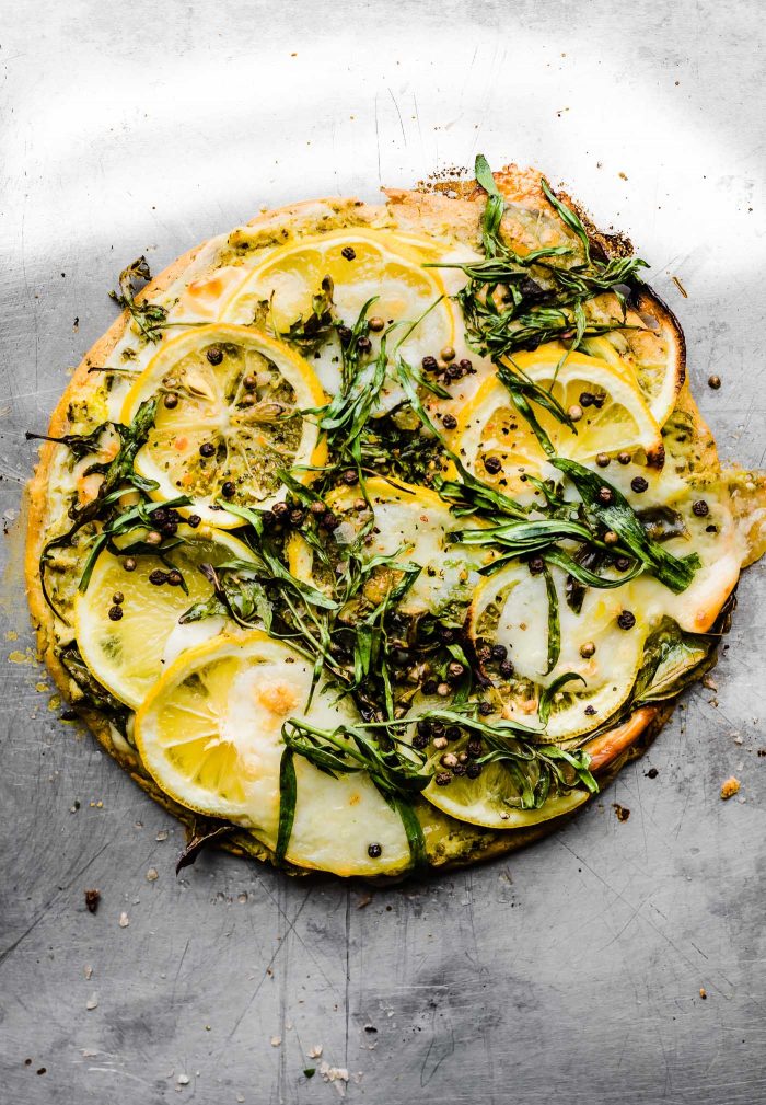 lemon herb socca pizza topped with mixed greens and lemon slices