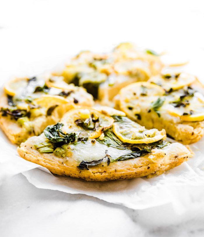 Flatbread pizza made with socca topped with lemon slices and fresh herbs, cut into slices.