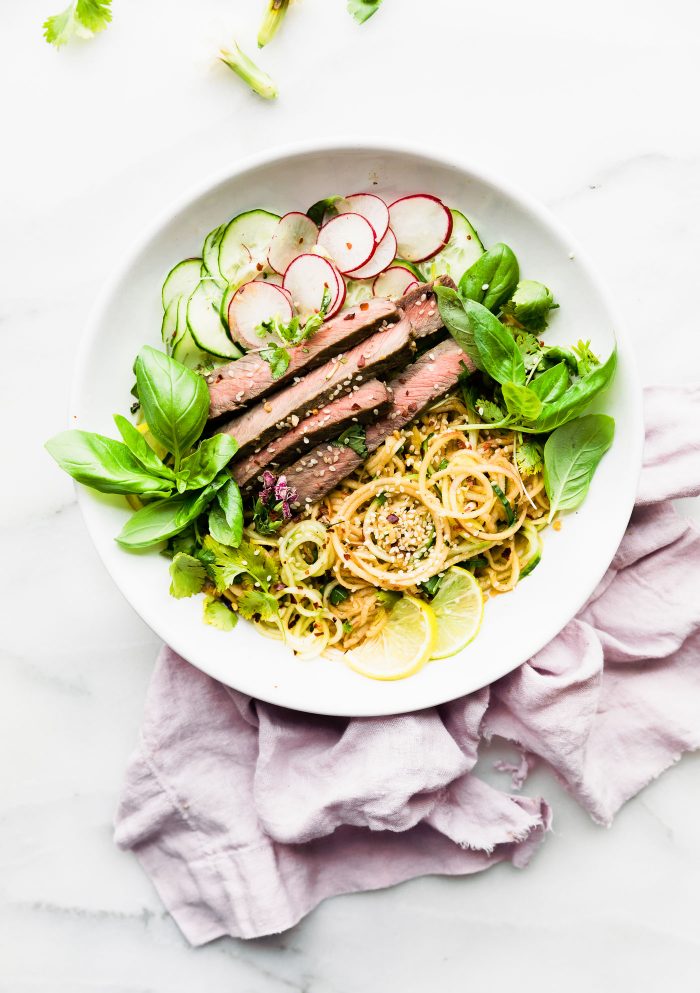 kimchi salad with sesame beef and spiralized vegetables on white plate.