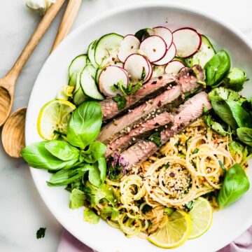 spiralized apple kimchi salad with beef served on white plate with fresh herbs on the side.