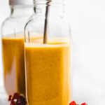 Two glass bottles filled with orange smoothie, metal straw in smoothies.