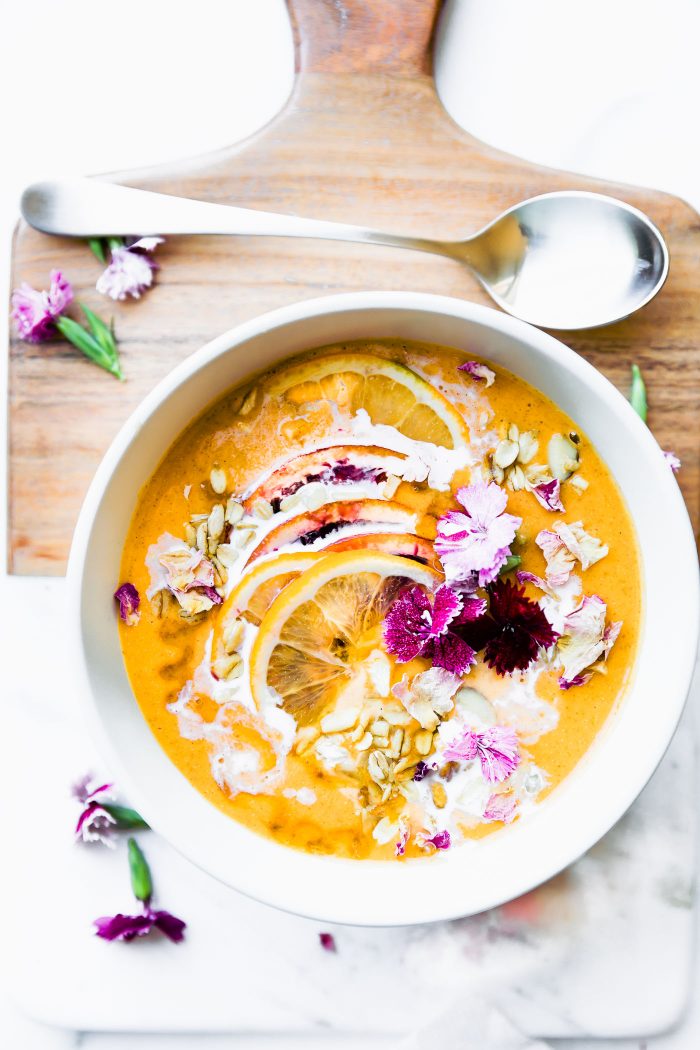Overhead view white bowl filled with orange immunity boosting smoothie bowl topped with orange slices and flowers.