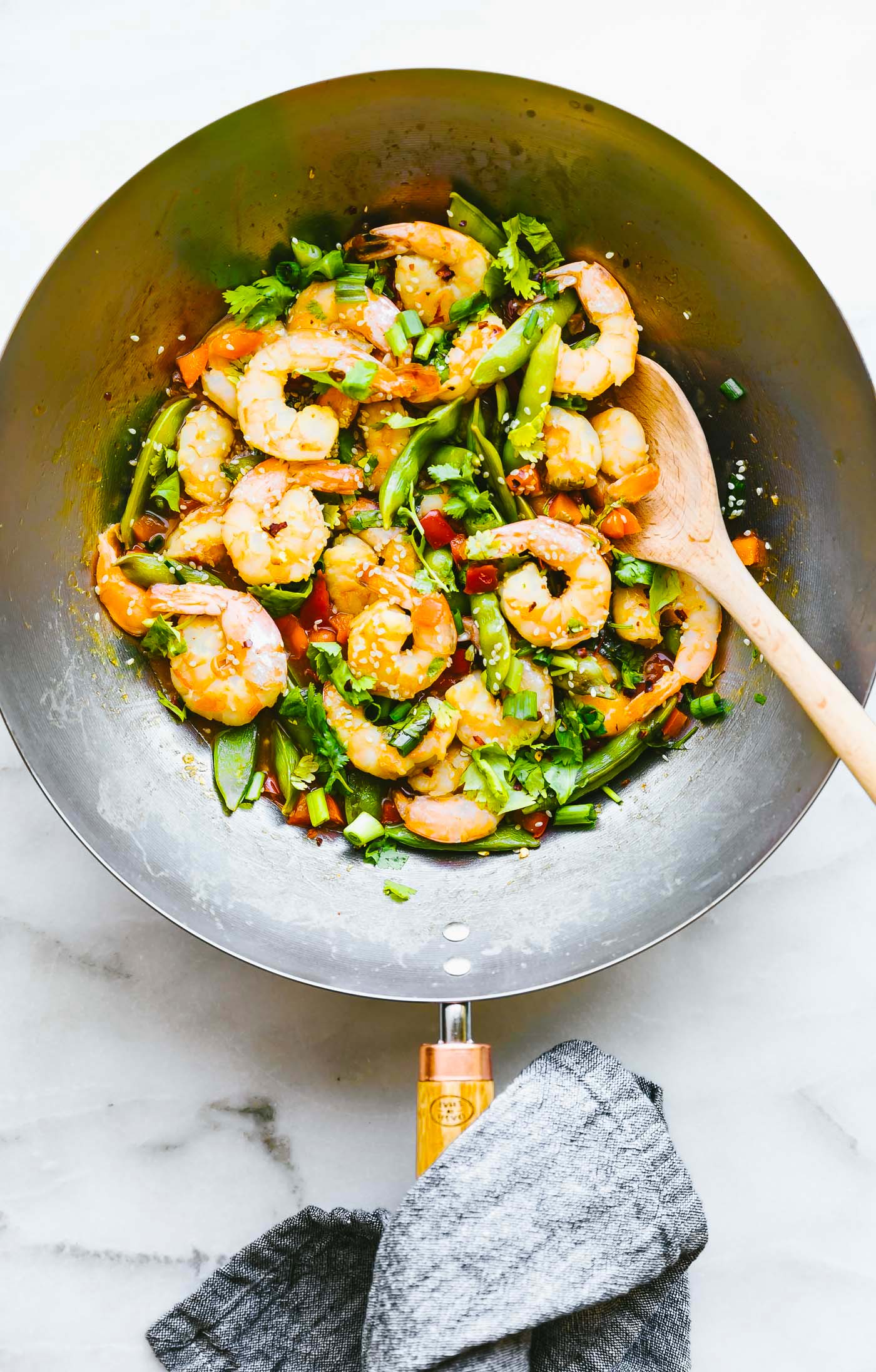 Overhead view wok-fired orange shrimp in a silver wok with wooden spoon.