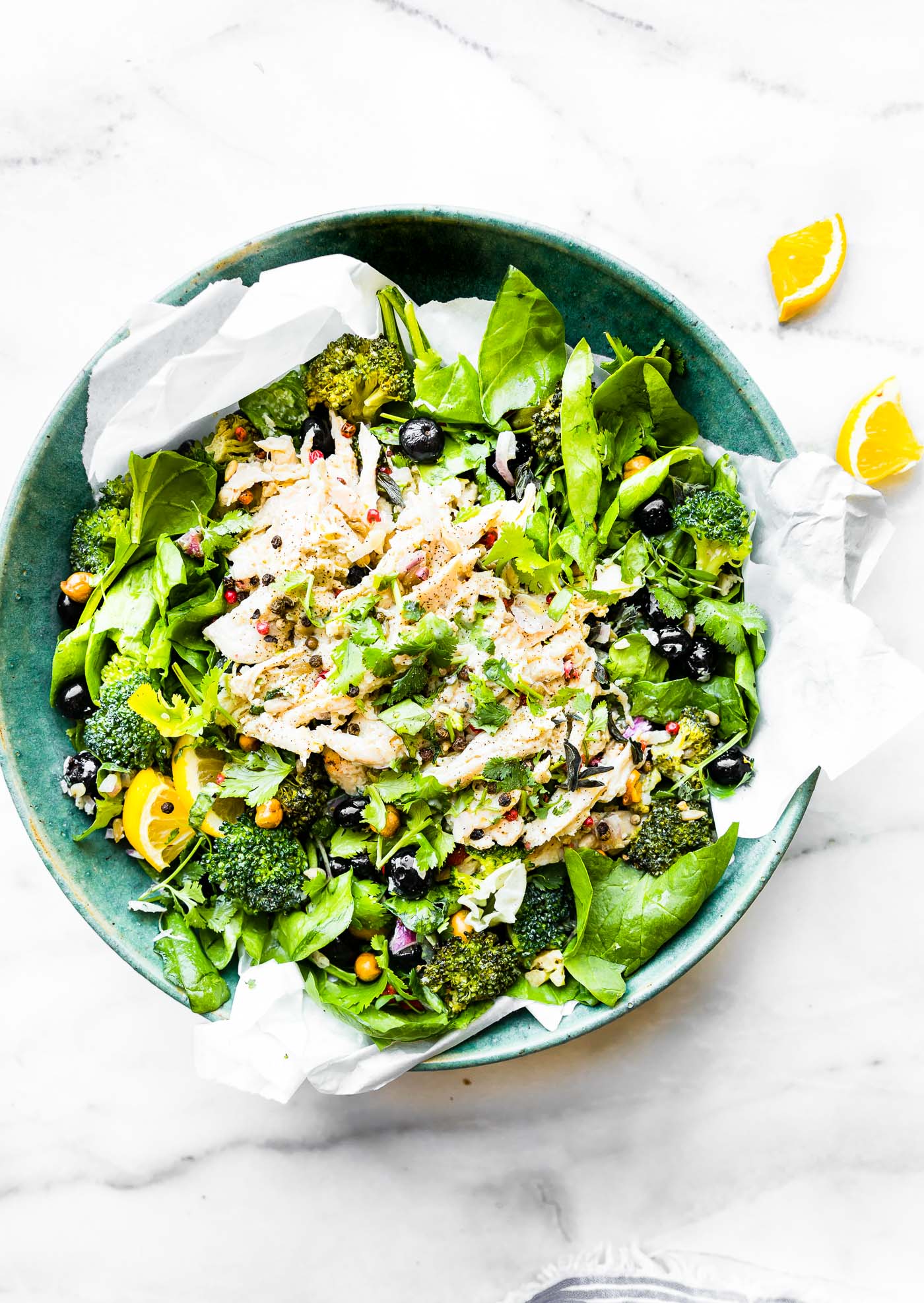 Overhead view turquoise bowl filled with chicken salad over mixed greens and broccoli.