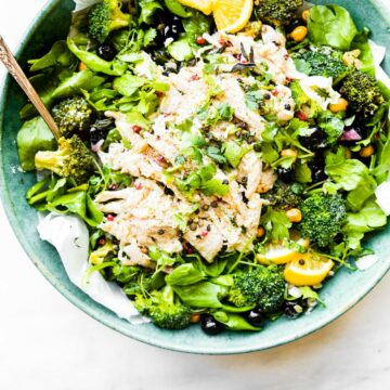 Turquoise bowl filled with shredded chicken salad over mixed greens and broccoli.