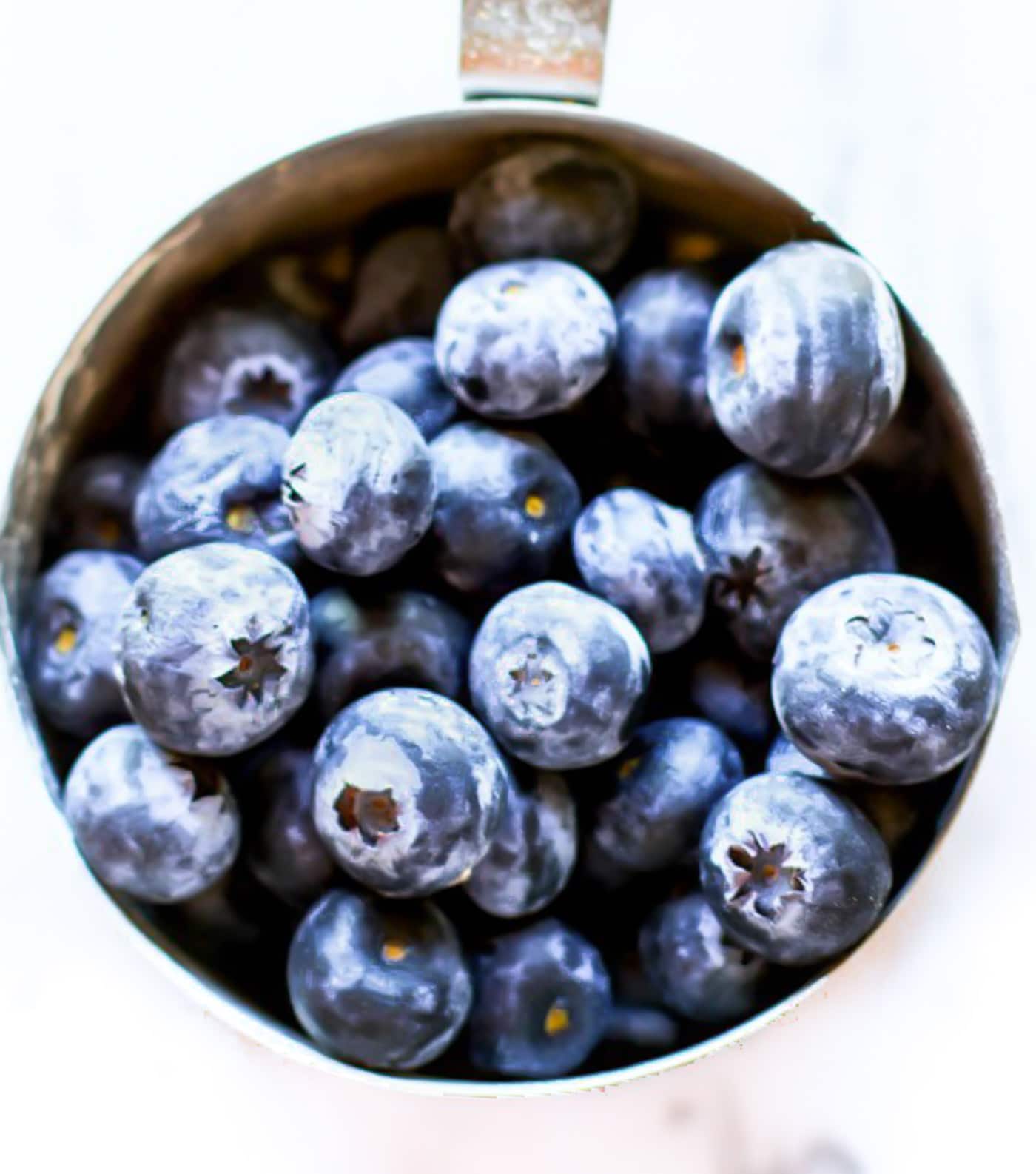 Overhead macro view fresh blueberries in silver measuring cup.