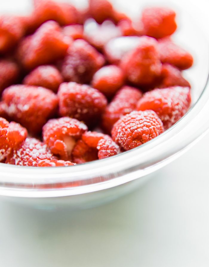 Close up view fresh raspberries in clear glass mixing bowl.