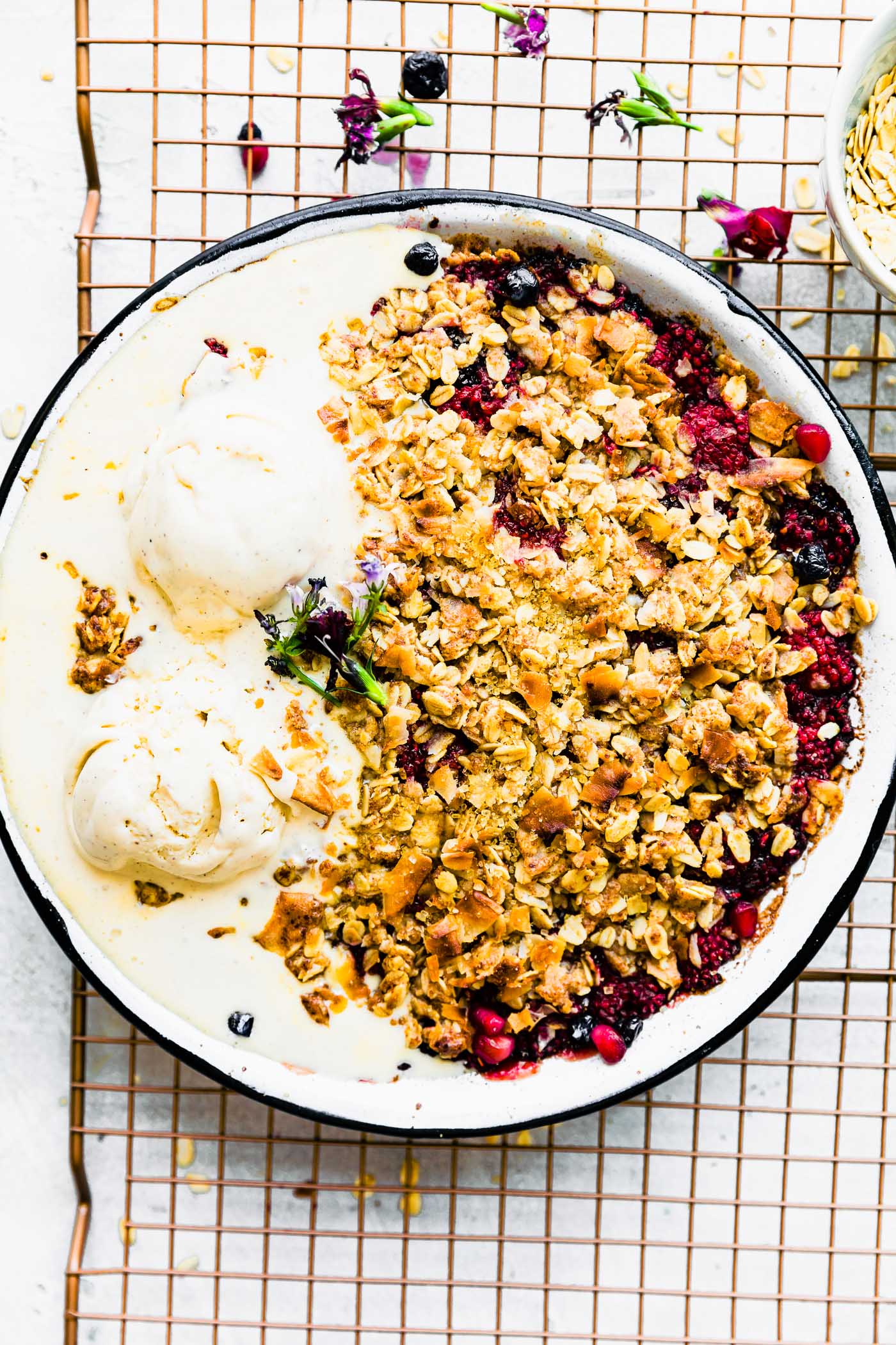 Overhead view coconut berry crisp in metal pie plate on wire cooling rack, melting ice cream on top of crisp