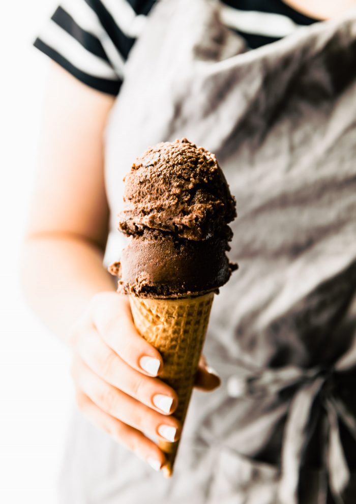 A hand holding an ice cream cone with espresso dark chocolate sorbet scoops on top.