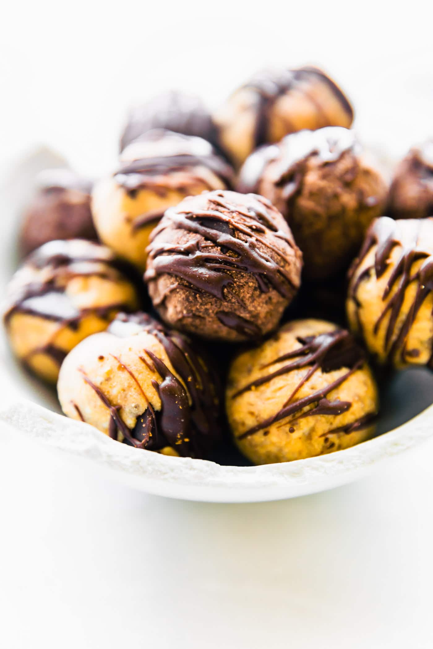 Bowl filled with dark chocolate protein bites, chocolate drizzled on top of each ball.