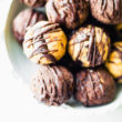 White bowl with several dark chocolate protein balls with chocolate drizzle piled high.