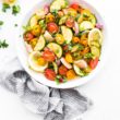 Full bowl of tomato zucchini salad with a striped napkin and dressing.