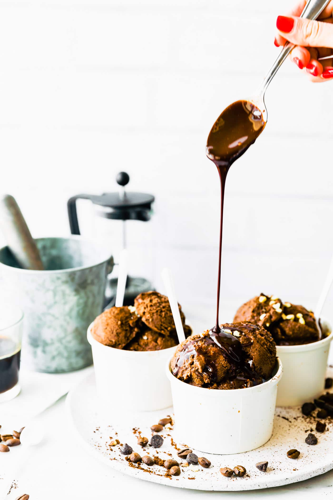 Melted dark chocolate being drizzled from spoon over double scoops of espresso dark chocolate sorbet in white paper bowls.