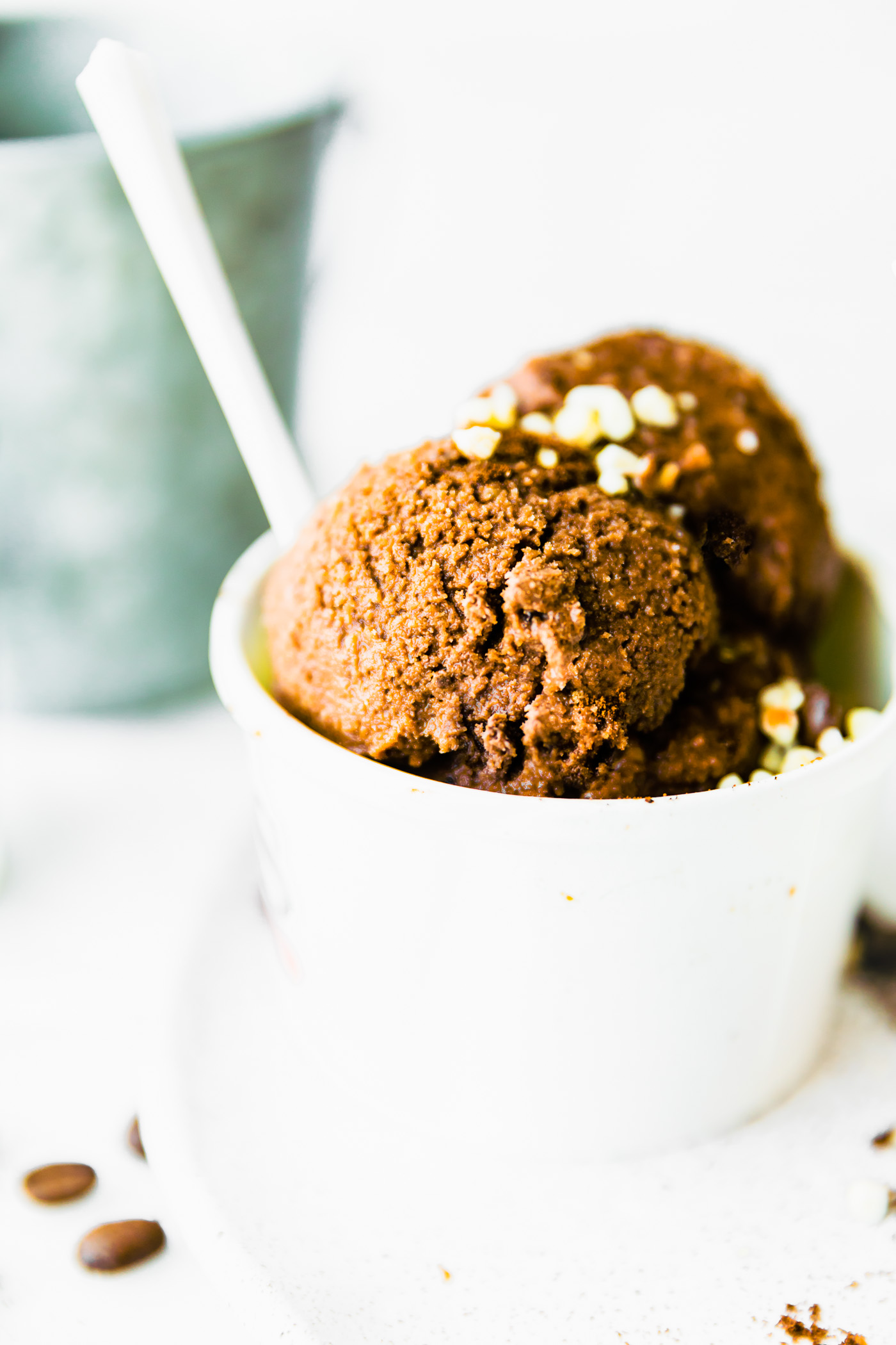 Close up dark chocolate espresso sorbet scoops in white paper bowl with white spoon.