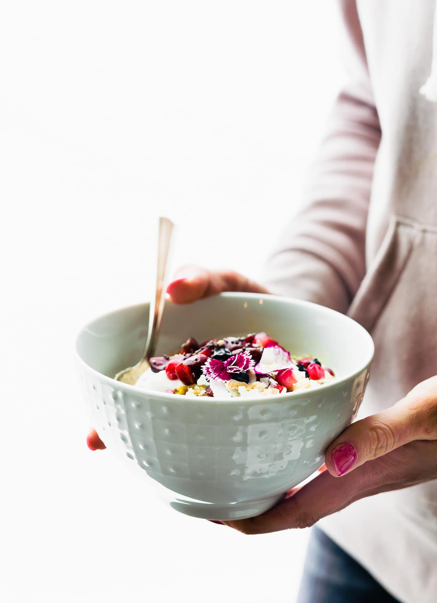 A woman holding a white bowl filled with AIP breakfast porridge topped with cream and fresh flowers.