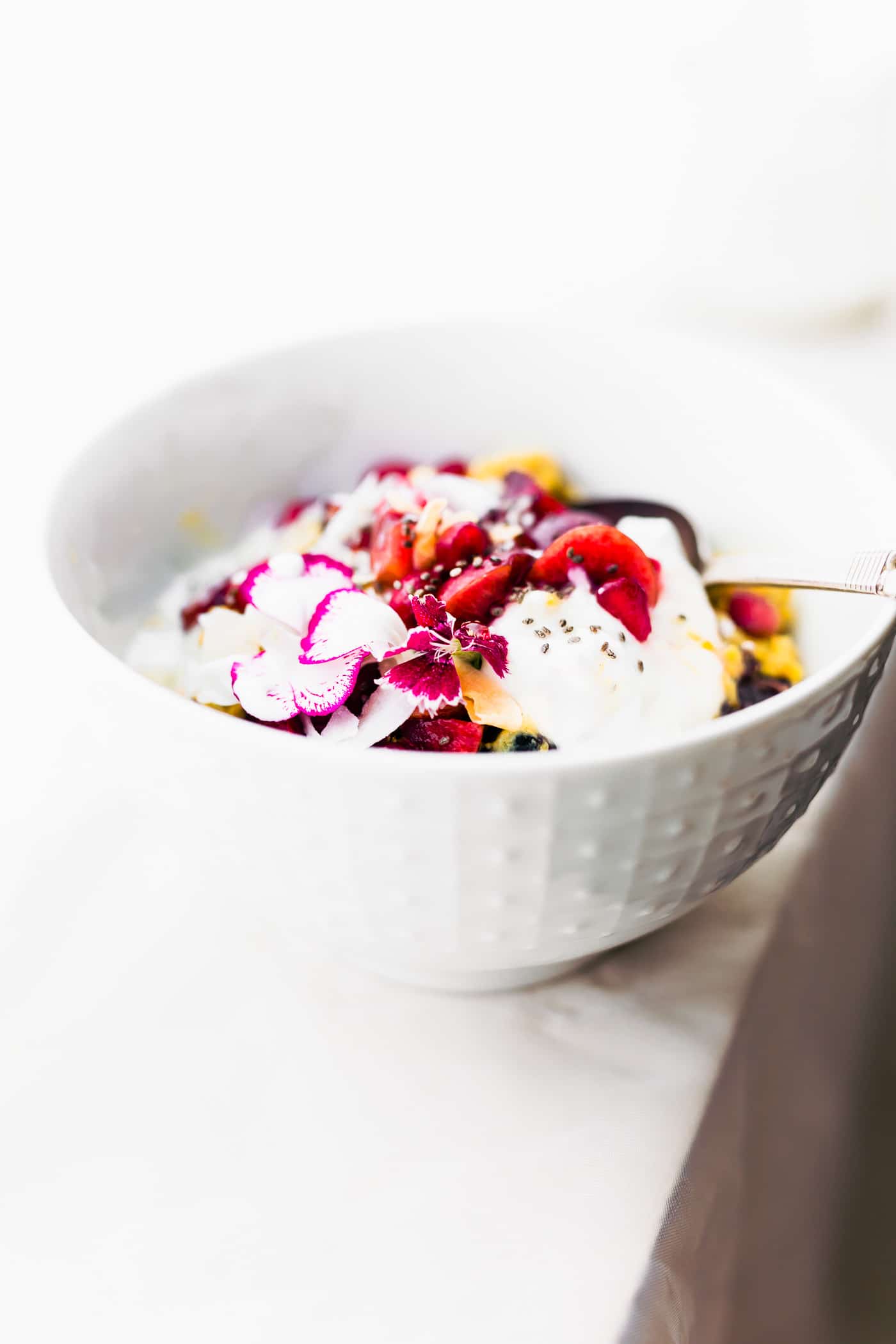 Healing breakfast porridge in white bowl topped with fresh fruit, cream, and fresh flowers.