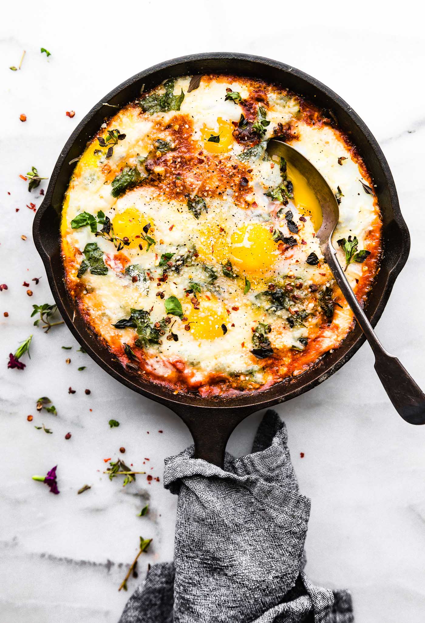 Overhead view small cast iron skillet filled with Italian egg bake topped with fresh oregano, spoon in egg bake