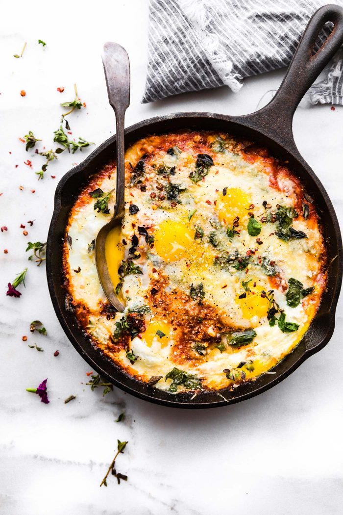 Italian Egg Bake prepared in a cast iron skillet. A serving spoon is scooping out some of the baked Italian eggs