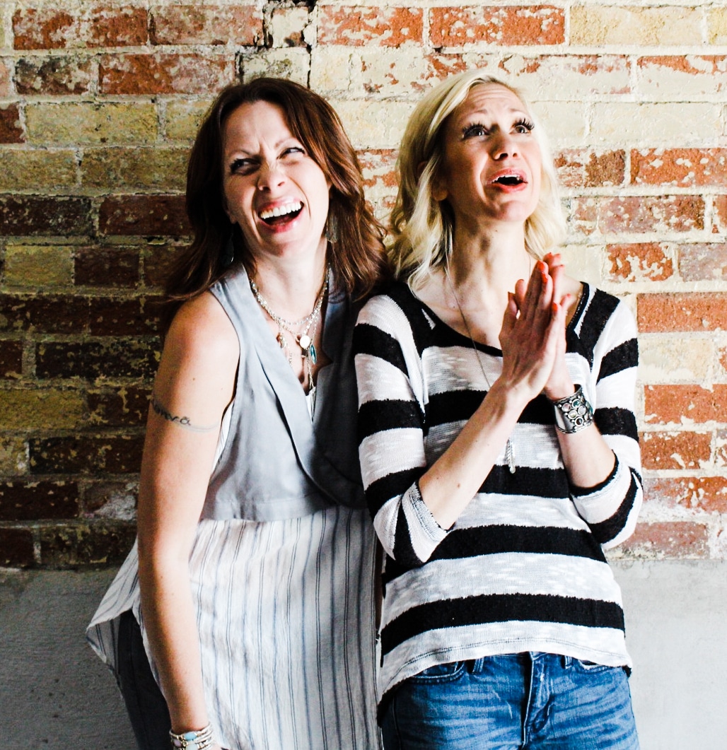 Two women against brick wall laughing