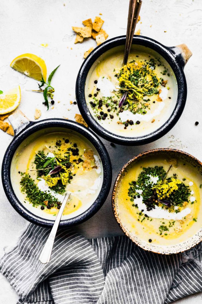 3 bowls of creamy roasted cauliflower soup with fennel topped with fresh herbs.