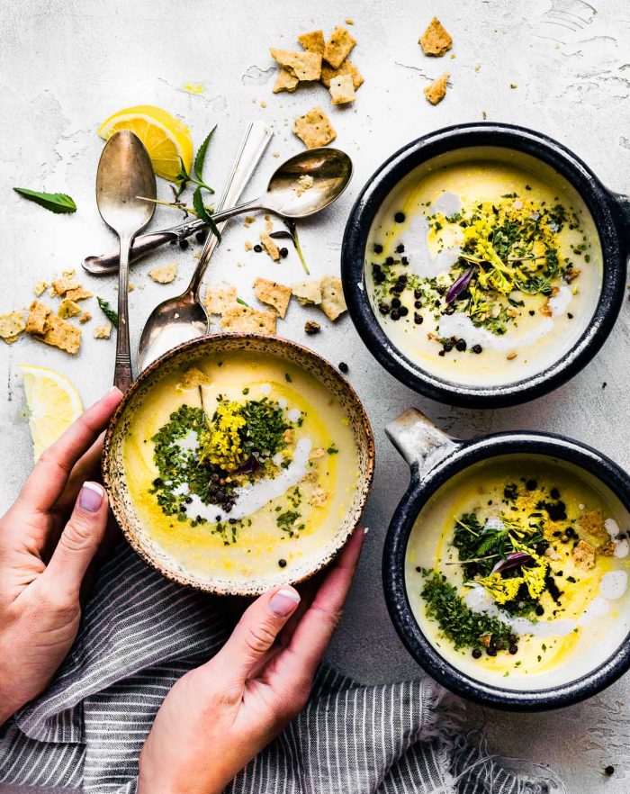 beautifully garnished bowls of creamy cauliflower soup garnished with fresh herbs, black peppercorns and a drizzle of olive oil