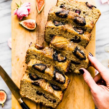 Almond flour loaf cake with honey roasted figs baked into top cut into thick slices on wooden cutting board.